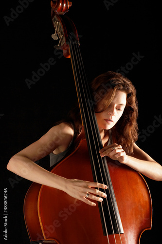 Young woman playing double bass against black background