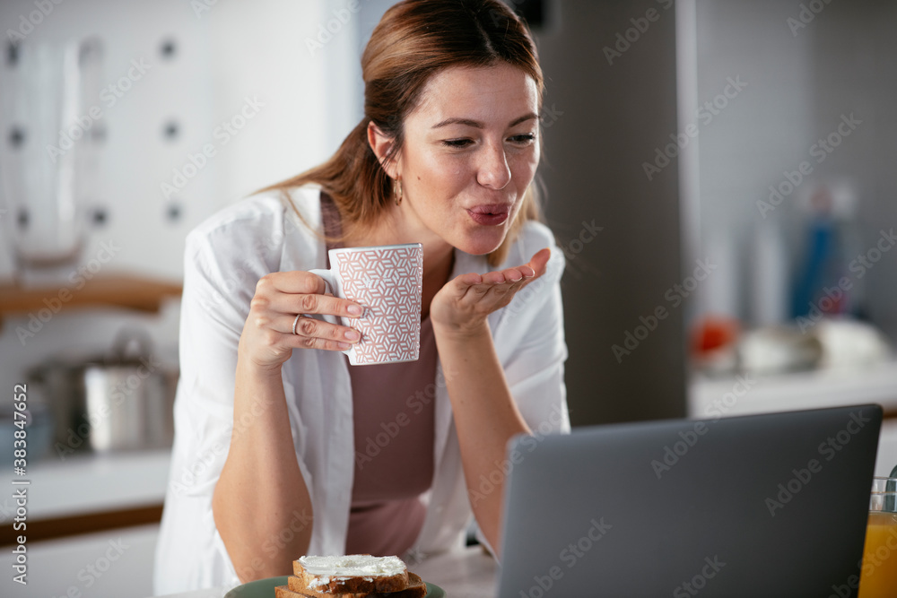 Beautiful woman eating breakfast in the kitchen. Young woman having video call
