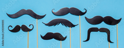 Various black photo booth props moustaches of different shape on blue background. Greeting card for father's day or men's health awareness month campaign concept. Flat lay, banner