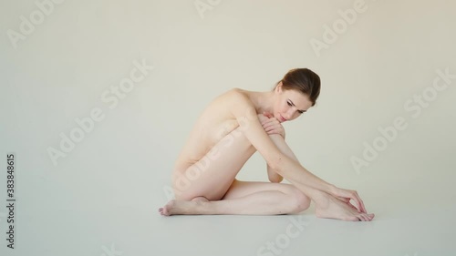 Young nude slim red-haired woman sits and touches the skin. Portrait of a naked skinny woman on a white background photo