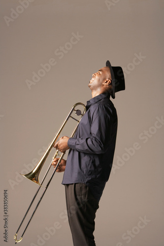 Fotografie Side view of a happy African American man with trombone standing against brown b