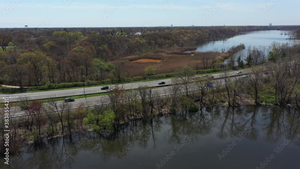 An aerial view of reflective lakes during the day. The drone camera tilts down while panning left over one of the lake. The parkway ahead has car traffic that is light. An aerial view of reflective lakes during the day. The drone camera tilts down while panning left over one of the lake. The parkway ahead has car traffic that is light.