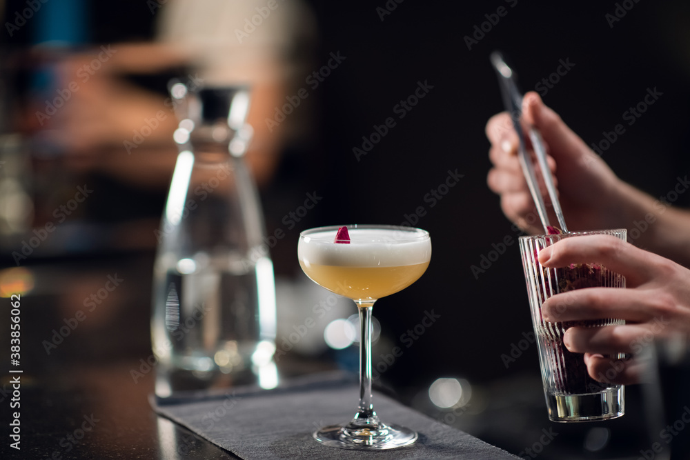 A glass with a bright yellow alcoholic cocktail on the bar and the hands of a bartender in a nightclub
