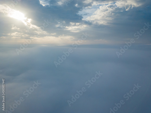 Aerial drone flight over the fog. There are thick clouds of fog below, the sun breaks through the clouds. © Sergey