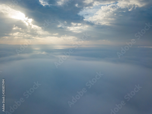 Aerial drone flight over the fog. There are thick clouds of fog below, the sun breaks through the clouds.