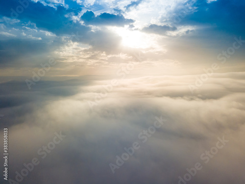 Fototapeta Naklejka Na Ścianę i Meble -  Aerial drone flight over the fog. There are thick clouds of fog below, the sun breaks through the clouds.