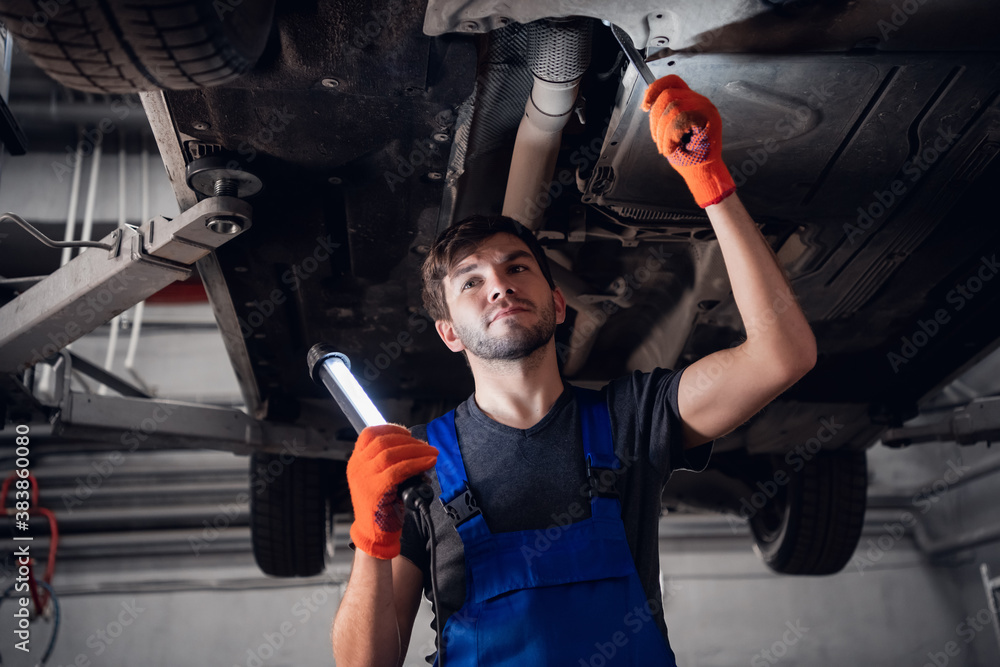 Engineer fixing car suspension and using a small flashlight