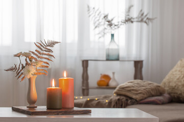 burning candles with autumn decor on white table at home