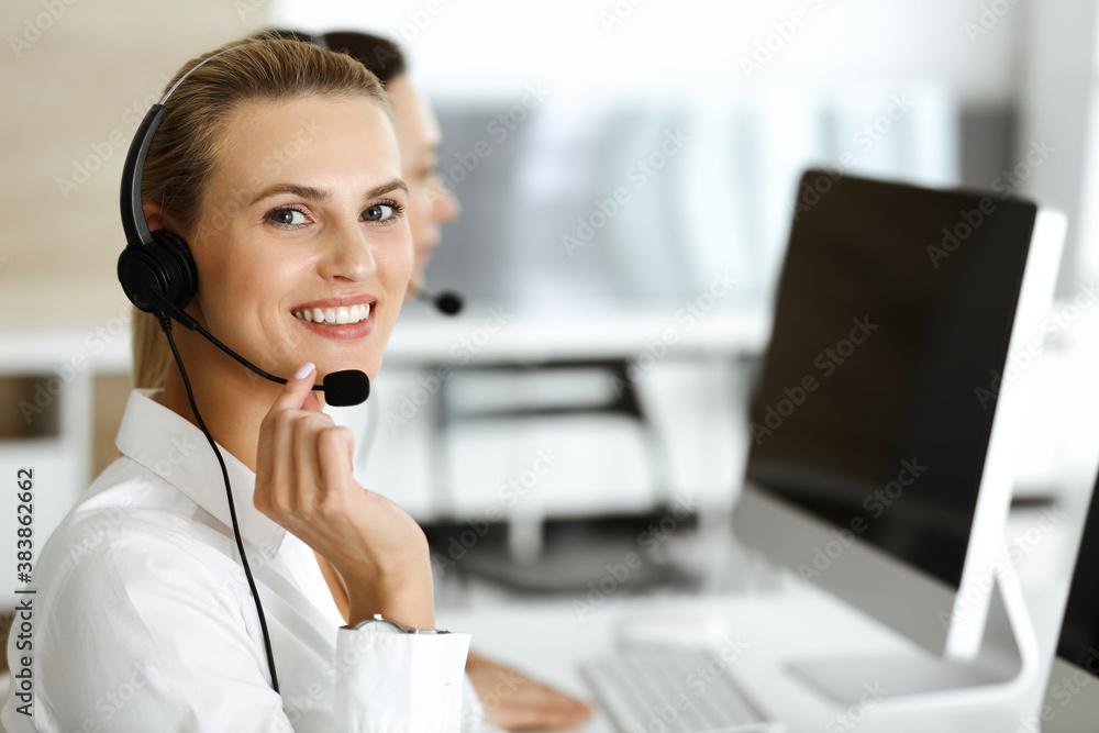 Blond female customer service representative and her colleague are consulting clients online using headset. Call center and business people concept Blond female customer service representative and her colleague are consulting clients online using headset. Call center and business people concept