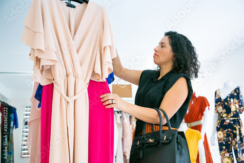 Focused fashion store customer choosing clothes and browsing dresses on rack. Medium shot, side view. Fashion store or retail concept