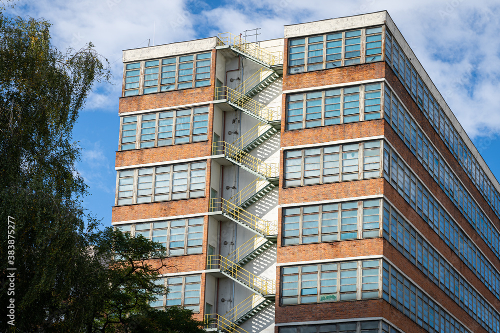 Exterior of a brick building from 1930s with emergency metal stairway. Large glass windows on a high rise building