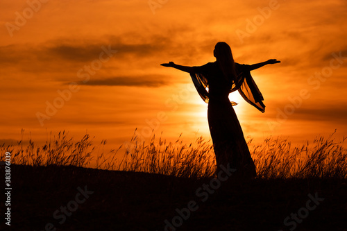 Silhouette of a woman with arms outstretched looking at beautiful sunset.