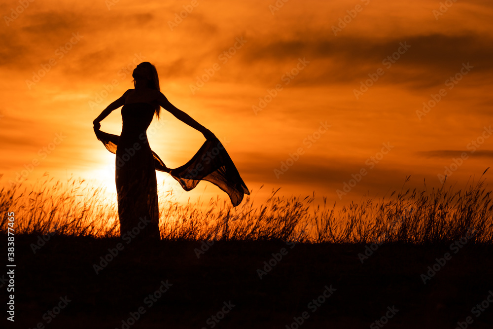 Happy woman dancing and holding scarf while enjoys spending time at sunset.