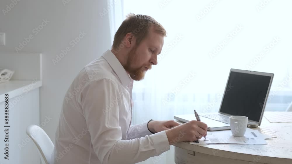 a man work at home behind a laptop by a bright window a man work at home behind a laptop by a bright window