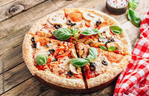 Sliced italian pizza with salami, mozzarella, mushroom, tomatoes, black olives and basil leaves on black background. Italian traditional food. Popular street food concept