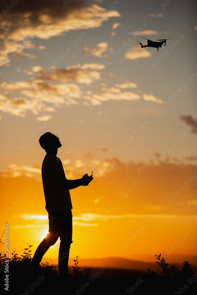 Fototapeta premium Silhouette of a man piloting a drone on A Rural Setting during sunset