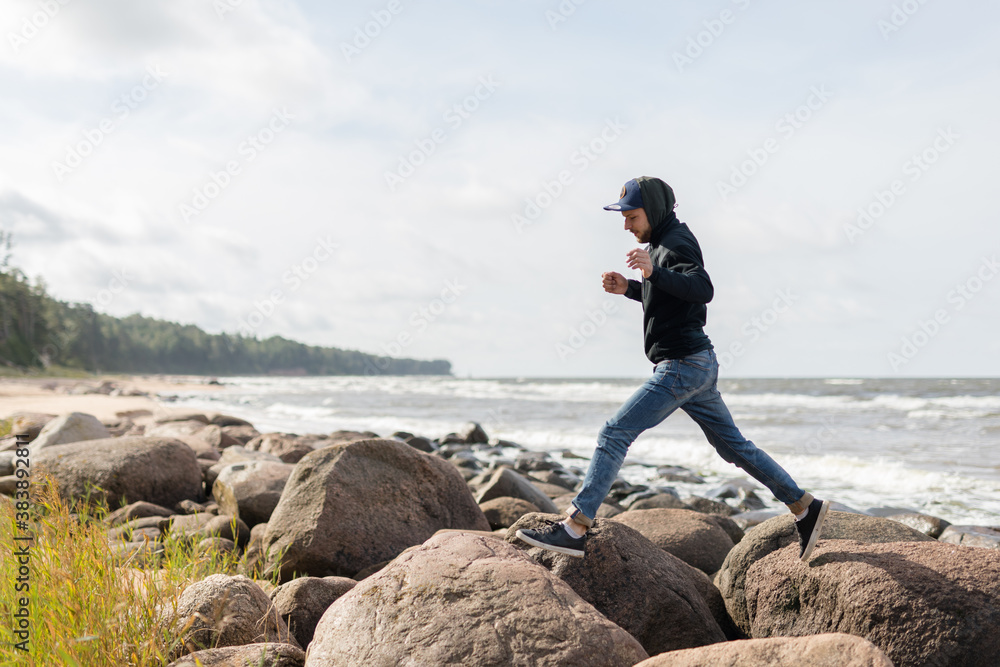 A young male having fun on the beachside of Baltic see, hopping from one large rock to another A young male having fun on the beachside of Baltic see, hopping from one large rock to another