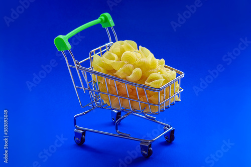 Pasta in the shape of seashells, mini supermarket cart filled to the top. Design for any purpose of advertising products. Blue background. photo