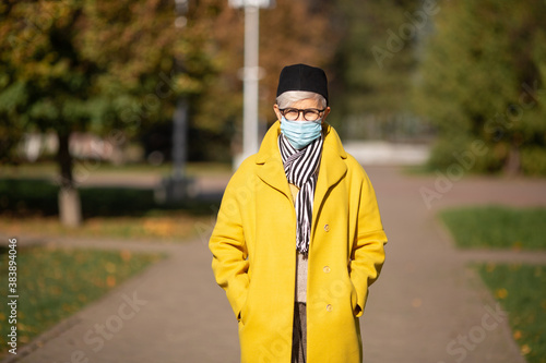 adult woman aged in the park in autumn in a medical face mask