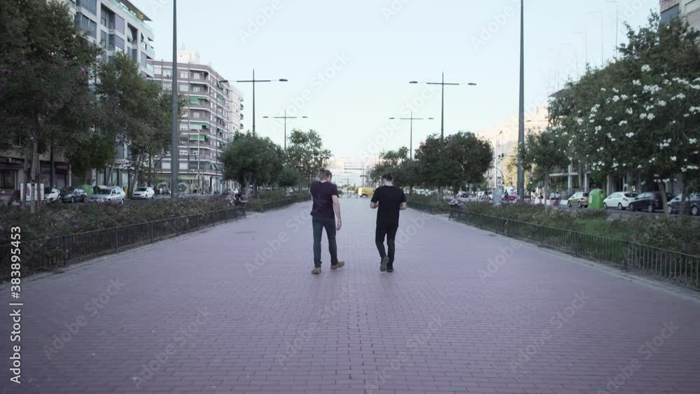 Two Hispanic Guys Smoking While Walking Together On A Concrete Pavement At The Urban Park During The Pandemic - Full-Body Shot Two Hispanic Guys Smoking While Walking Together On A Concrete Pavement At The Urban Park During The Pandemic - Full-Body Shot