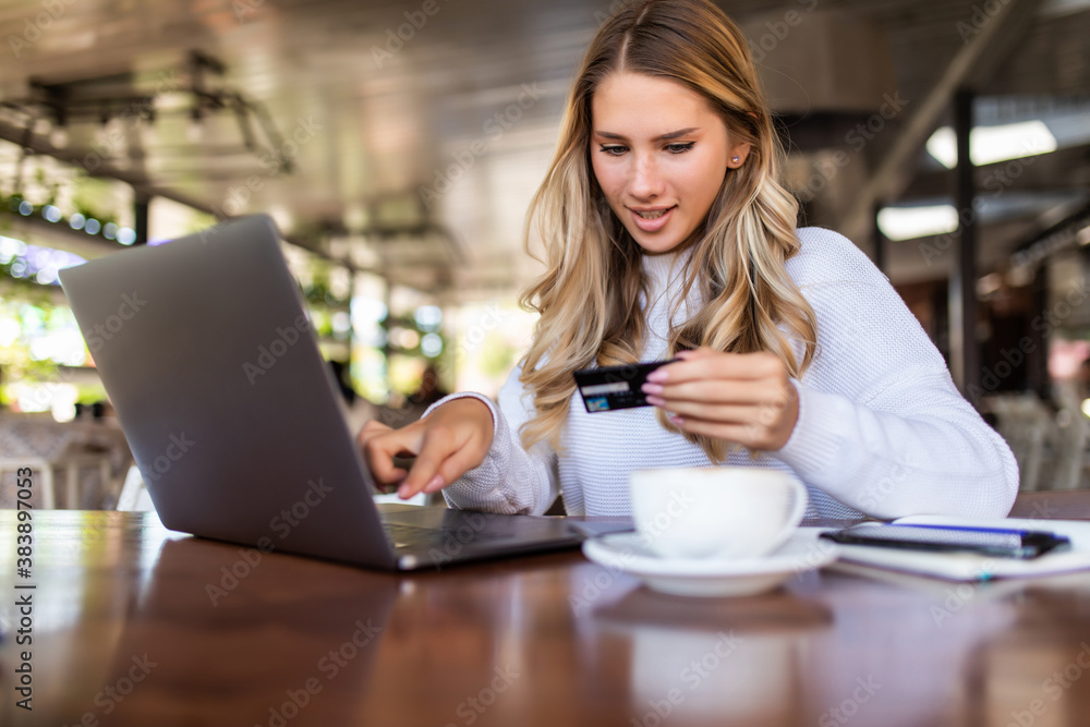 Happy young woman using credit card and laptop for shopping while sitting in cafe. Happy young woman using credit card and laptop for shopping while sitting in cafe.