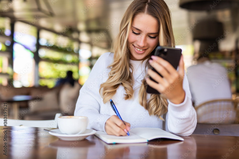 Cheerful young woman talk phone conversation on smartphone doing order and making notes of information about delivery. Positive hipster girl calling on mobile phone sitting with coffee Cheerful young woman talk phone conversation on smartphone doing order and making notes of information about delivery. Positive hipster girl calling on mobile phone sitting with coffee