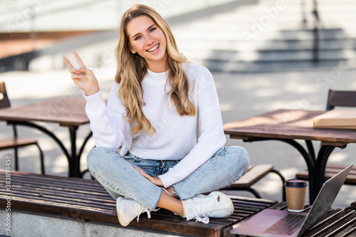 Happy young woman giving the peace sign sitting in a urban bench