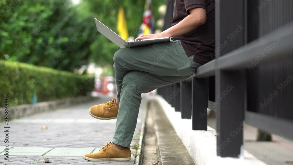 Young man using his laptop on fence relaxing. Young man using his laptop on fence relaxing.