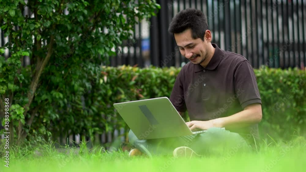 Asian young man using his laptop on a lawn. Asian young man using his laptop on a lawn.