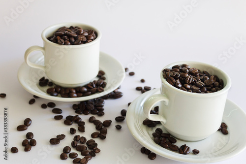 Roasted coffee beans in two coffee cups , on white isolated background.
