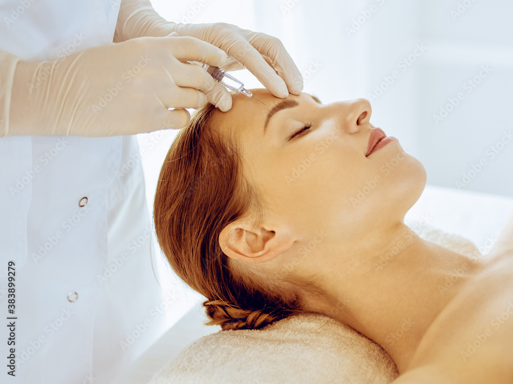 Beautiful woman receiving beauty injections with closed eyes in medical center. Beautician doctor hands doing beauty procedure to female face with syringe