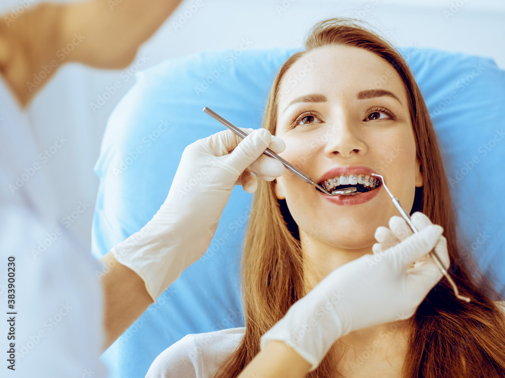 Smiling young woman with orthodontic brackets examined by dentist in dental clinic. Healthy teeth and medical care concept Smiling young woman with orthodontic brackets examined by dentist in dental clinic. Healthy teeth and medical care concept