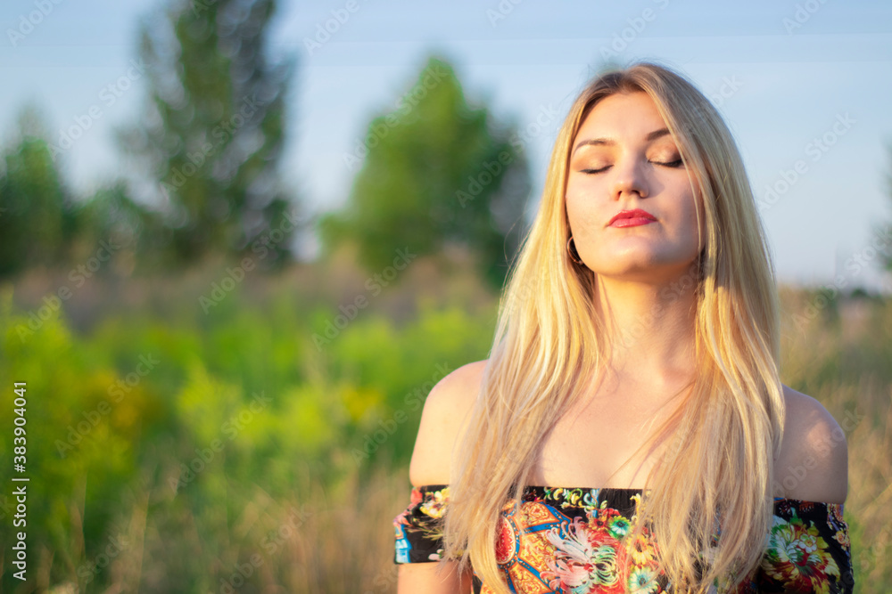 Naklejka premium overlight bright portrait of a charming attractive blonde in flowery dress in the field. 