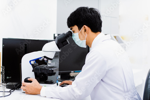 young medical technician look at the microscope in medical laboratory