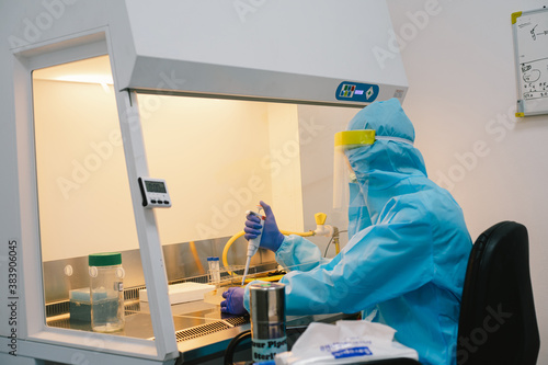 A scientist in PPE safty uniform pipetting sample experiment in biological safety cabinet (BSC).