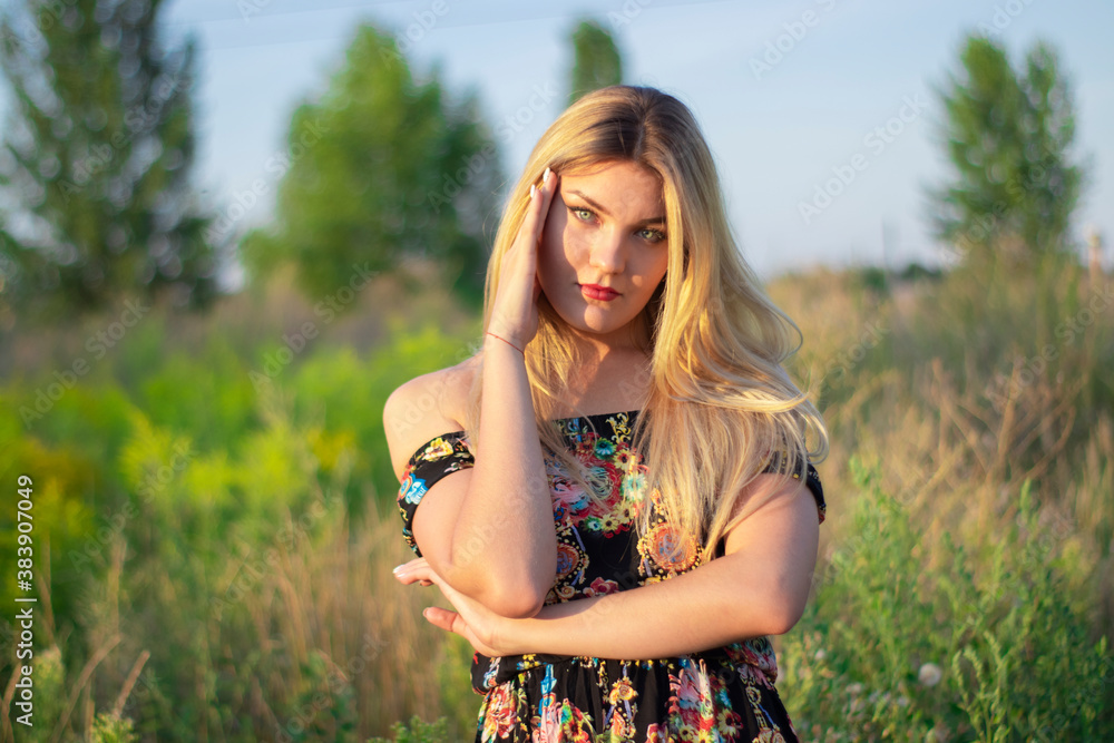 overlight bright portrait of a charming attractive blonde in flowery dress in the field. overlight bright portrait of a charming attractive blonde in flowery dress in the field.
