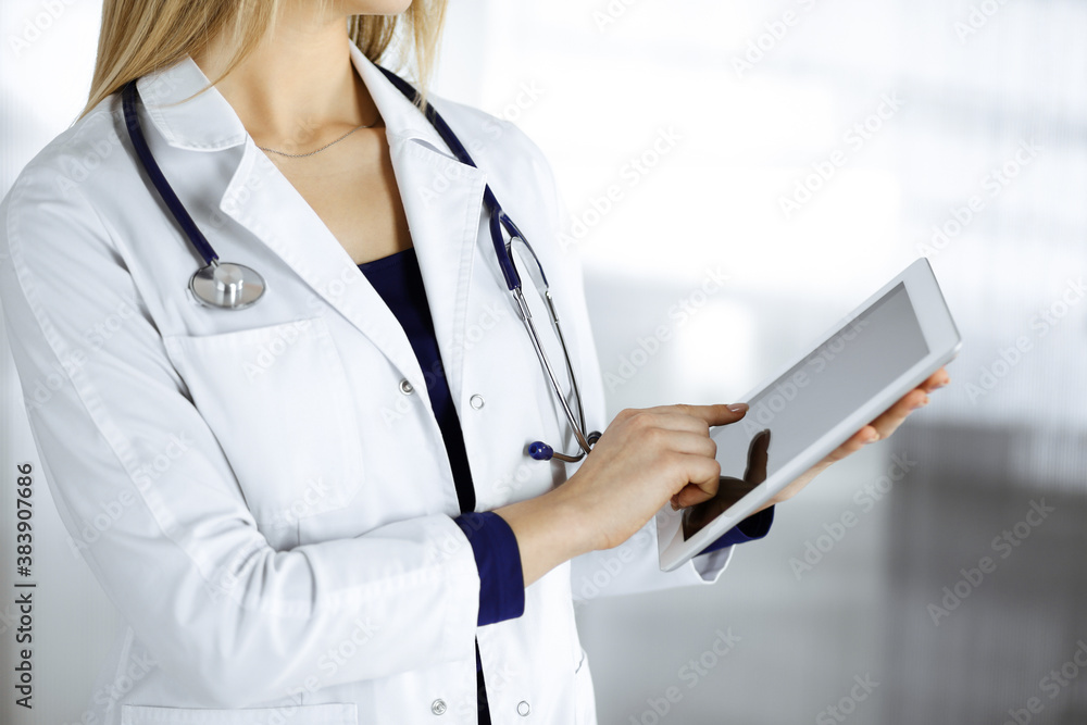 Unknown woman-doctor is holding a tablet computer in her hands, while standing in a clinic cabinet. Female physician at work, close-up. Perfect medical service in a hospital. Medicine concept Unknown woman-doctor is holding a tablet computer in her hands, while standing in a clinic cabinet. Female physician at work, close-up. Perfect medical service in a hospital. Medicine concept