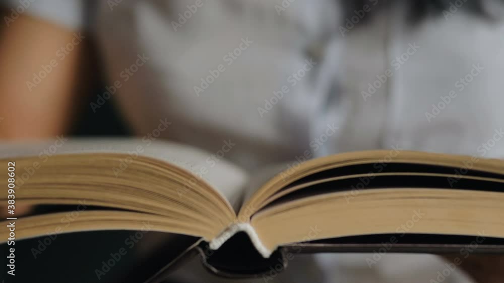 Brunette in blurred white blouse hand turns book page of yellow colour under bright light sitting at home slow motion extreme closeup Brunette in blurred white blouse hand turns book page of yellow colour under bright light sitting at home slow motion extreme closeup