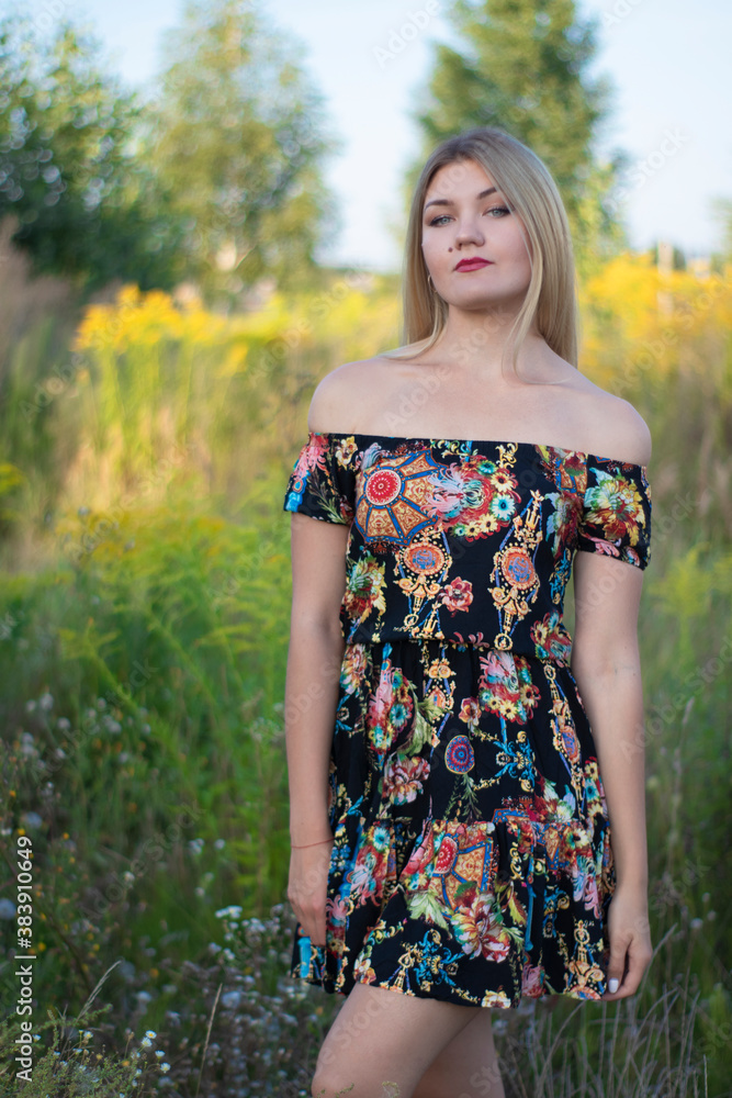 Fototapeta premium overlight bright portrait of a charming attractive blonde in flowery dress in the field. 