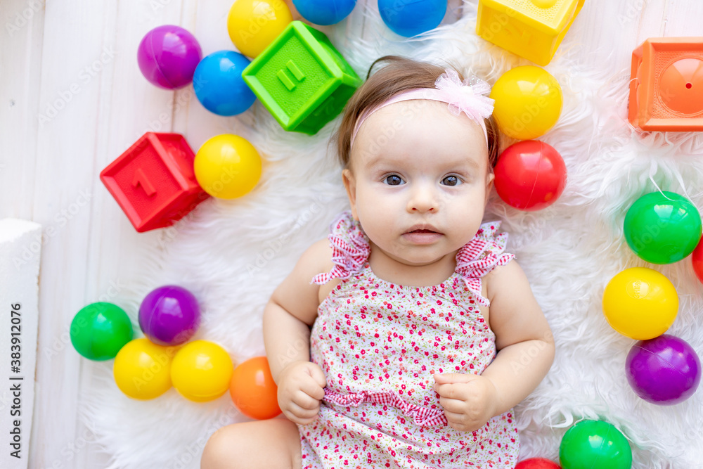a beautiful little baby girl is lying in red clothes on a white Mat among toys balls and cubes a beautiful little baby girl is lying in red clothes on a white Mat among toys balls and cubes