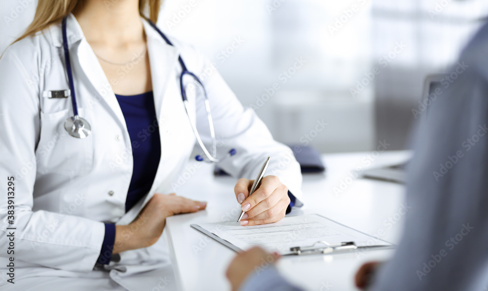 Unknown woman-doctor is prescribing some antibiotics for her patient, while they are sitting at the desk in the cabinet in a clinic. Female physician with a stethoscope is writing at clipboard, close Unknown woman-doctor is prescribing some antibiotics for her patient, while they are sitting at the desk in the cabinet in a clinic. Female physician with a stethoscope is writing at clipboard, close