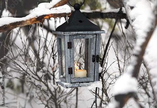 Lantern with a candle hanging on a tree in the winter forest.