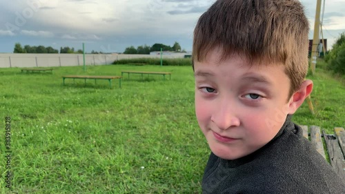 A boy sitting on a bench on a children playground, looking in a camera and making funny faces using his eyebrows