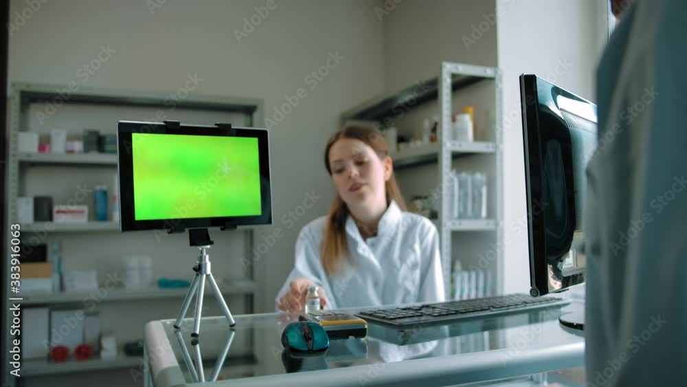 Green screen tablet on pharmacy showcase with woman, presenting vaccine ampoule. Place for pasting Your content after 3d tracking for medicines commerce. Female talking with male customer. Green screen tablet on pharmacy showcase with woman, presenting vaccine ampoule. Place for pasting Your content after 3d tracking for medicines commerce. Female talking with male customer.