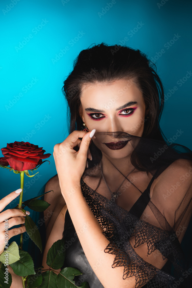 evil bride with dark makeup holding rose and veil on blue