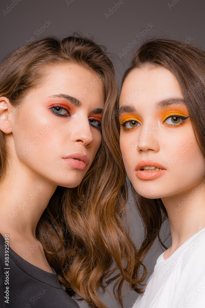 Two beautiful attractive girls with bright red and orange make-up stand on a gray background Two beautiful attractive girls with bright red and orange make-up stand on a gray background