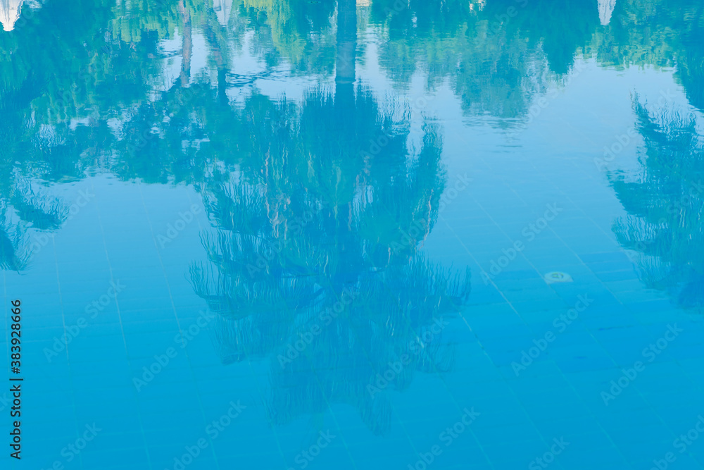 Fototapeta premium Reflections of palm trees in the calm blue water of a swimming pool conceptual of tropical summer vacations and travel