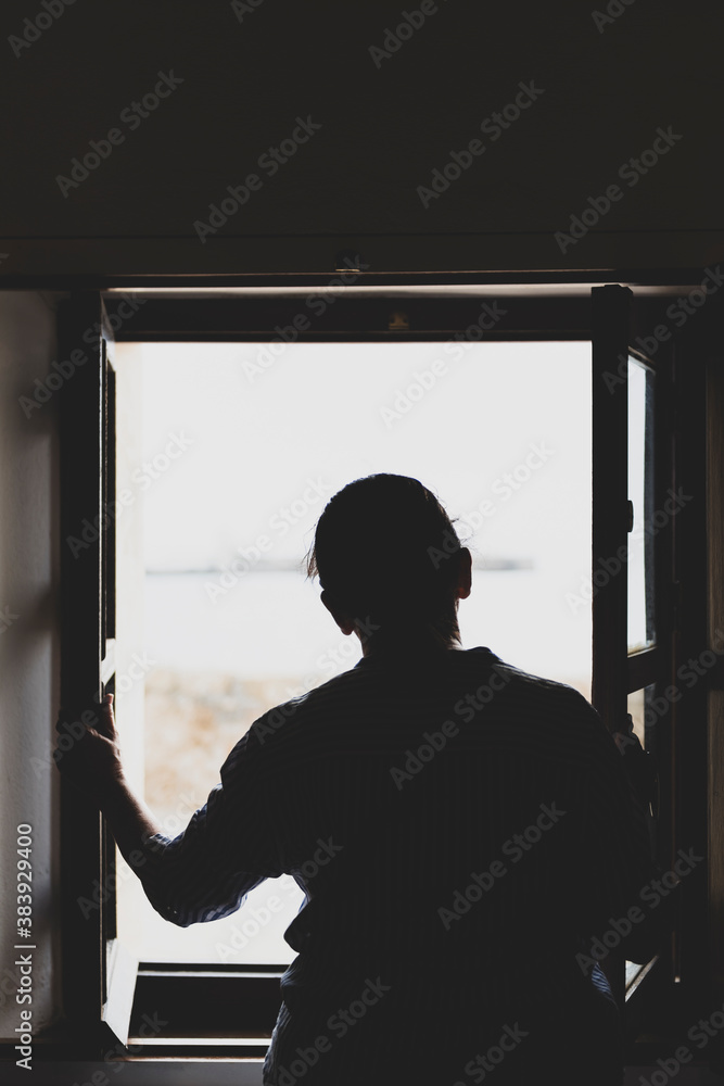 Silueta de contraluz de una mujer mirando por la ventana