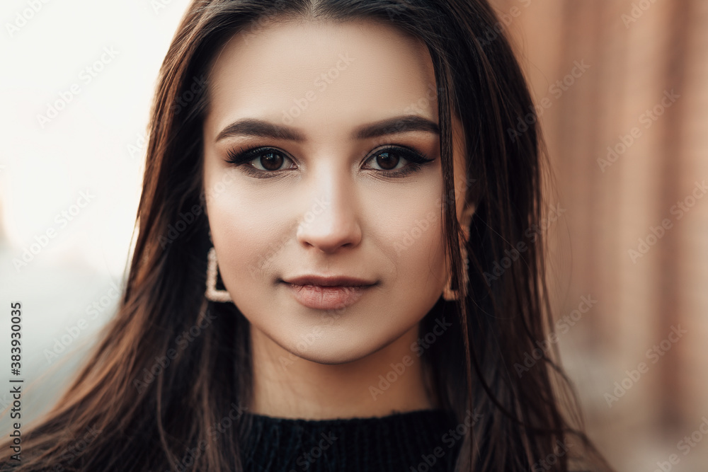 Naklejka premium Close up lifestyle portrait of young indian woman is cold standing on the street cloudy weather, dressed in black pullover and looking at the camera. 