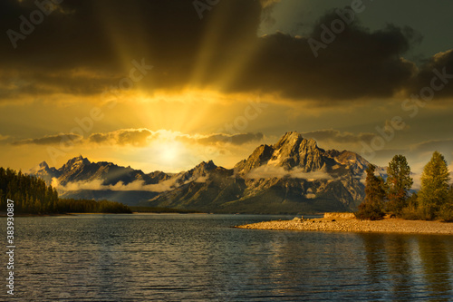 Sun setting with storm clouds over a lake with tall mountains